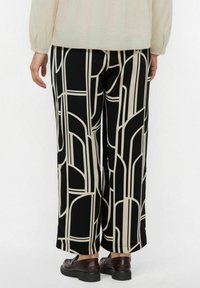 Pantalones anchos negros con patrones geométricos blancos, hechos de una tela suave. Presentan una silueta limpia y un dobladillo recto. Combinados con zapatos oscuros.