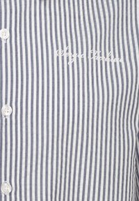 Blue and white striped cotton shirt with a button-down front and logo embroidered in script across the chest. Smooth texture, regular fit.