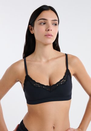 Bralette in pizzo nero con spalline regolabili, scollo profondo e design senza cuciture con un bordo in pizzo lavorato a trama lungo i bordi.