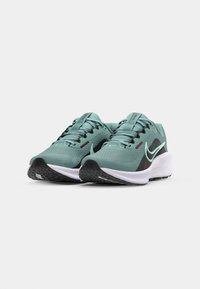 Grüne und schwarze Sportschuhe mit einer strukturierten Oberseite, weißem Zwischensohlenbereich und Gummilaufsohle. Mit schwarzen Schnürsenkeln und einem Swoosh-Logo.
