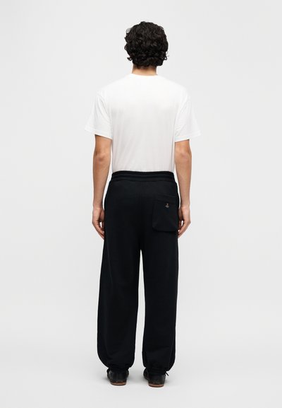 Μαύρο βαμβακερό παντελόνι φόρμας με χαλαρή εφαρμογή, ελαστική μέση και πίσω τσέπη. Συνδυασμένο με ένα απλό λευκό T-shirt.
