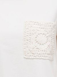 Gros plan sur un tissu blanc avec une poche carrée en crochet présentant un motif floral circulaire sur la partie supérieure du torse.