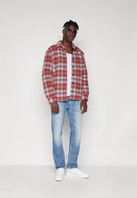 Raudonos ir mėlynos spalvų languota flanelinė marškiniai, balti marškinėliai be rankovių, šviesiai mėlyni džinsai ir balti sportbačiai. Aksesuarai: tamsūs akiniai nuo saulės.