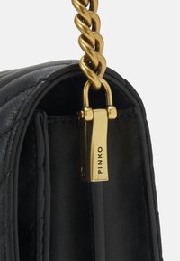 Borsa in pelle nera con texture trapuntata, dotata di una tracolla in catena dorata intrecciata e di una chiusura in metallo dorata con l'etichetta "PINKO."