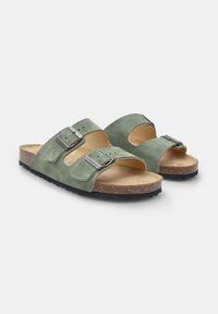 Gröna mockaskinnsandaler med två justerbara spännen, en formad fotbädd i naturlig kork och en strukturerad gummiyttersula. Öppen tå-design.