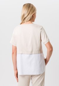 Korte mouwen top met een beige bovenkant en een witte onderpaneel. Gladde textuur, rechte snit en subtiele naden bij de taille.