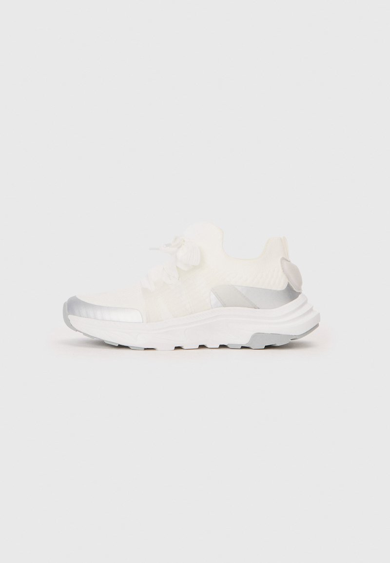 White athletic sneaker with textured upper, metallic silver accents on the sides and toe, and a cushioned sole. Laces tied in a bow.