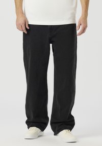 Črne kavbojke iz džinsa z ravnim krojem, s čistim zaključkom in minimalističnim slogom. Kombinirane z belimi športnimi supergami.