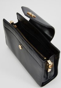 Černá kožená psaníčko s texturovaným povrchem, zlatým kováním, zacvakávacím uzávěrem a vnitřní kapsou na zip. Otevřený design odhaluje přihrádky.