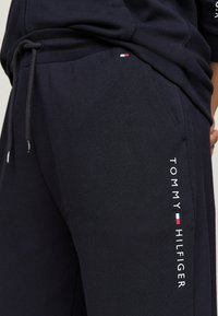 Navy Jogginghose aus weichem Stoff, mit einem Kordelzugbund, Seitentasche und dem "TOMMY HILFIGER"-Logo in Weiß mit Farbakzenten.
