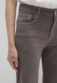 Gray corduroy pants with ribbed texture, featuring front pockets and a button closure at the waistband. Close-up view of fit and fabric.