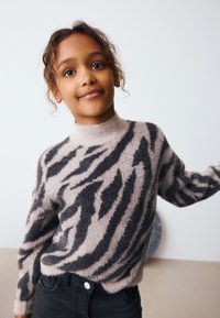 Knitted sweater in blush pink with black zigzag stripes. Features a high neck and long sleeves, made from a soft, fuzzy material.