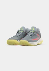 Egy pár szürke sportcipő sárga talppal, neon zöld logóval a nyelvén, és piros swoosh mintával az oldalán, fehér háttér előtt.