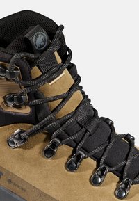 Nahaufnahme eines hellbraunen Wildleder-Wanderschuhs mit schwarzer gepolsterter Zunge, schwarzen runden Schnürsenkeln, Metallösen und atmungsaktivem Mesh-Kragen.