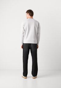 Felpa grigia chiara con scollatura tonda, abbinata a jeans neri larghi e sneakers bianche con suole beige.