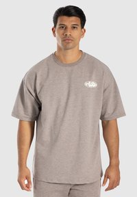 Grå kortærmet t-shirt lavet af blødt stof, med rund halsudskæring og et hvidt logo på venstre brystområde.