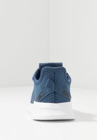 Zapatilla deportiva con una parte superior de malla azul, una suela de goma blanca y una pestaña trasera texturizada. Presenta un acabado suave y acentos mínimos.