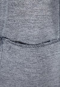 Šedá texturovaná tkanina s měkkým tkaním, obsahující viditelný šev a detaily kapsy. Celkově hladký vzhled s jemnou barevnou variací.