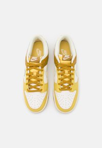 Sneakers Nike cechują się żółto-białym skórzanym wzorem z perforowanym czubkiem, wyściełanym kołnierzem i żółtymi sznurowadłami. Płaska podeszwa z subtelnym brandingiem.