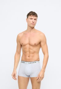 Grå bomullsboxere med en svart og blå "Lacoste" logo på midjen, som har en tettsittende design og glatt tekstur.