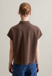 Braunes Polo-Shirt mit kurzen Ärmeln, strukturiertem Stoff und abgerundetem Saum, kombiniert mit blauen Denim-Jeans mit Gesäßtaschen.