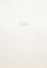 Balta medvilninė marškinė su švelnia tekstūra, ant krūtinės centruotoje vietoje esantis šviesiai bežinis logotipas, kuris skelbia "lala BERLIN".