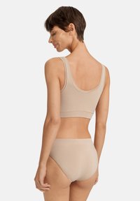 Beige sömlös bralette och högmidjade trosor, med slät yta och breda axelband, visade bakifrån mot en enkel bakgrund.