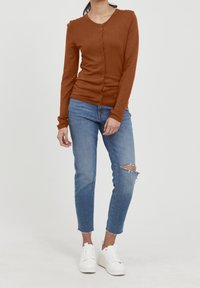 Brun långärmad cardigan med rund halsringning och knäppning, tillsammans med ljusblå slitna jeans och vita sneakers.