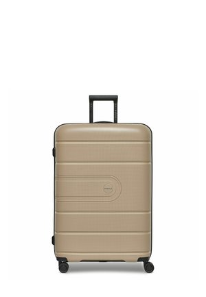 Valise rigide de couleur beige claire avec une finition texturée, des accents noirs, quatre roues pour la mobilité et une poignée rétractable.