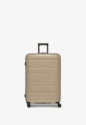 Valigia rigida color beige chiaro con finitura testurizzata, dettagli neri, quattro ruote per la mobilità e manico retrattile.