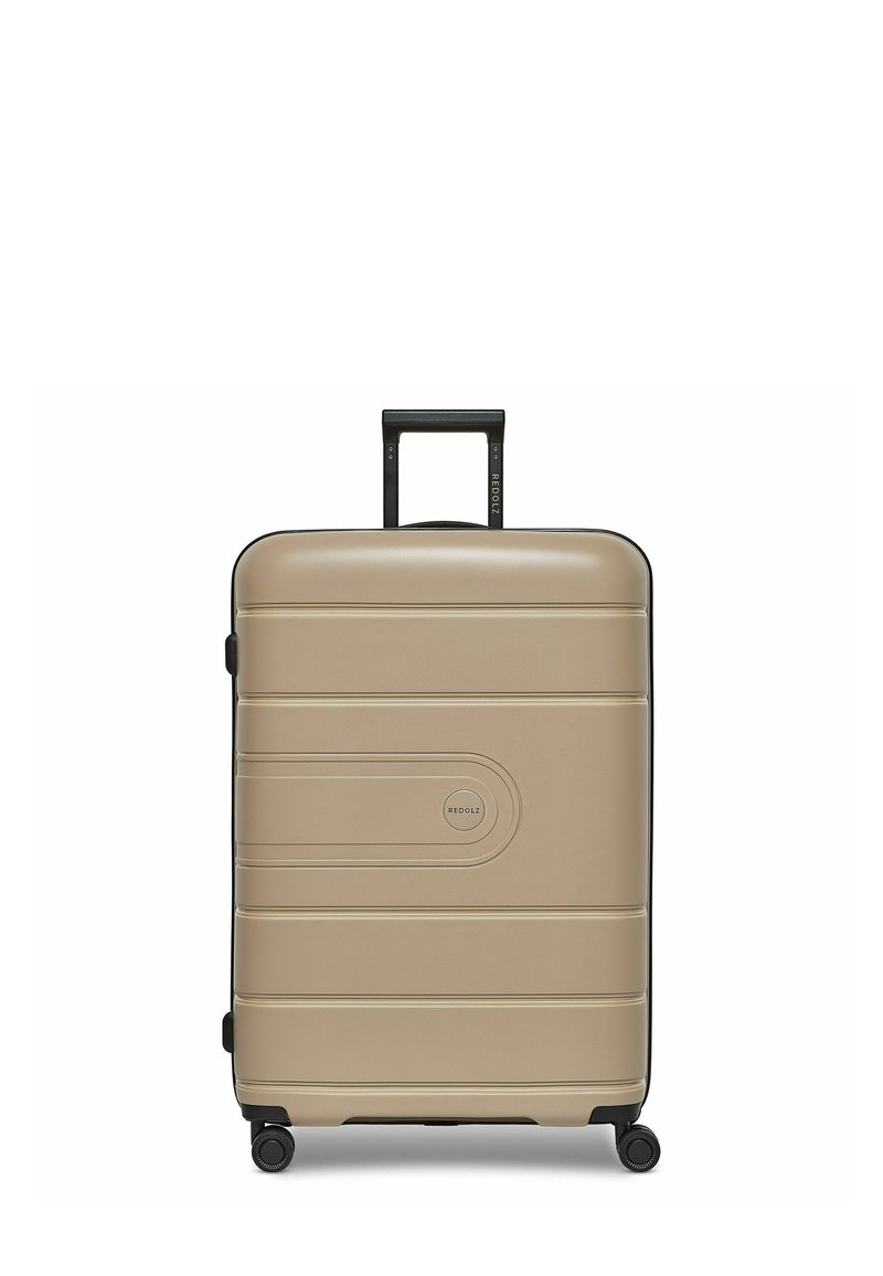 Valigia rigida color beige chiaro con finitura testurizzata, dettagli neri, quattro ruote per la mobilità e manico retrattile.