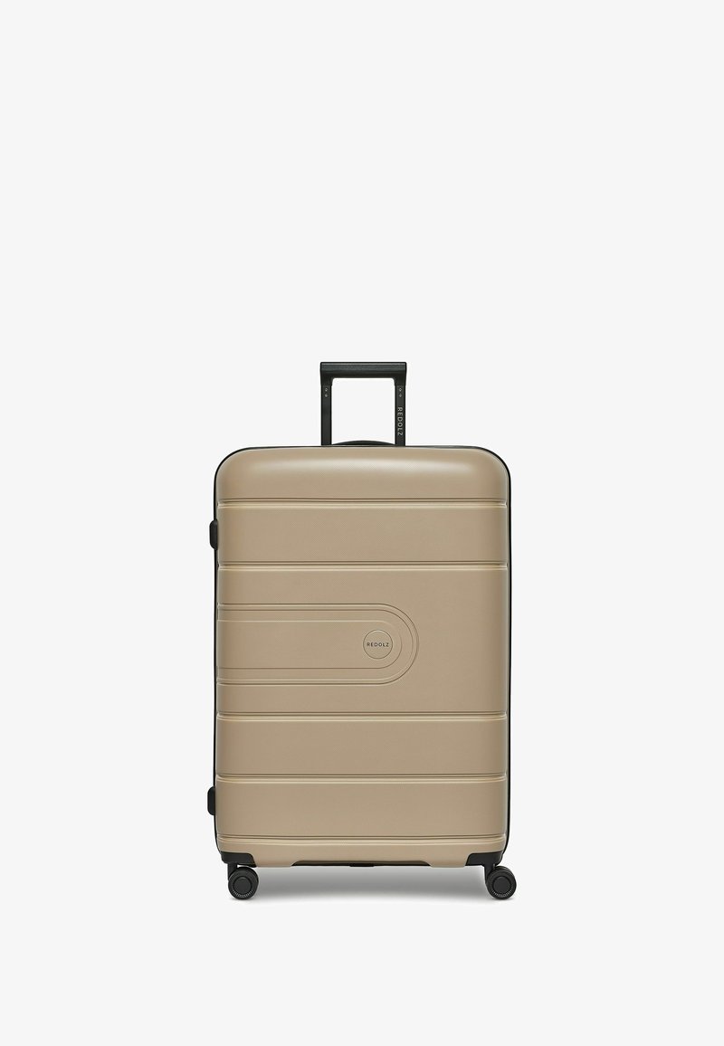 Harde koffer in lichtbeige met een gestructureerde afwerking, zwarte accenten, vier wielen voor mobiliteit en een uitschuifbare handgreep.