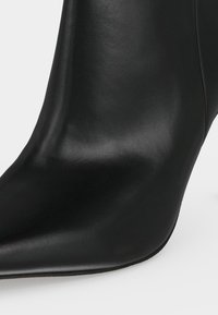 Gros plan d'une bottine en cuir noir avec un bout pointu et une finition lisse.