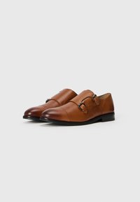 Zapatos de cuero marrón con un acabado liso, detalles de doble hebilla, puntera redondeada y un tacón bajo. Sutil degradado tonal en la zona de los dedos.