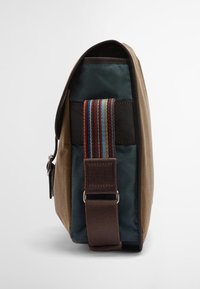 Καφετί τσαντάκι αγγελιοφόρου με πράσινο εσωτερικό, διαθέτοντας ρυθμιζόμενο λουρί πολλαπλών ρίγων, λεία υφή και λεπτομέρεια κλεισίματος στο πλάι.