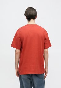 Κόκκινο βαμβακερό μπλουζάκι με άνετη εφαρμογή, κοντά μανίκια και στρογγυλή λαιμόκοψη. Απλό σχέδιο με ομαλή υφή, ορατό από πίσω.