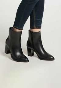 Stivaletti neri in pelle, con punta appuntita e cerniera laterale. Tacco alto e spesso, con una texture liscia e dettagli di cucitura visibili.