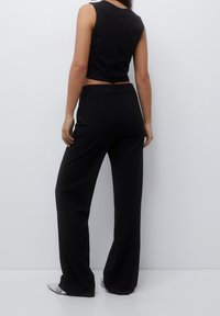 Svart ribbad crop top i kombination med högmidjade svarta vida byxor, med en mjuk tygtextur och minimalistisk design.