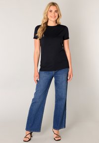 Slim-fit marineblauw T-shirt met korte mouwen gecombineerd met high-waisted, wijd uitlopende blauwe jeans en zwarte sandaaltjes met bandjes. Glad stofje, casual stijl.