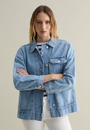Giacca in denim azzurro chiaro con colletto, tasca frontale e chiusure a bottone. Presenta una vestibilità leggermente oversize e dettagli di cucitura visibili.