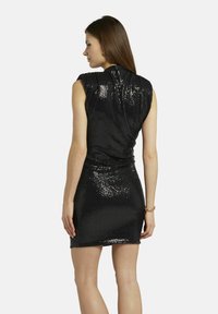 Robe noire sans manches avec une silhouette ajustée, recouverte de sequins brillants, et un dos drapé, atteignant mi-cuisse.
