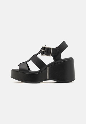 Sorte wedge-sandaler med bred stropdesign, justerbar spænde og tekstureret platform. Glat læder og kontrasterende syninger.