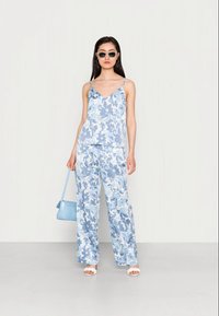 Conjunto de estampa floral azul claro, composto por uma blusa de alças finas e calças de perna larga. Inclui uma pequena mala azul e sandálias brancas tipo slide.