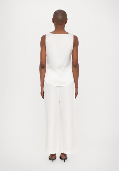 Valkoinen hihaton toppi yhdistettynä leveälahkeisiin valkoisiin housuihin, molemmat sileäpintaisia. Yhdistetty mustiin korkokenkiin.