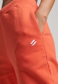 Oranga sweatpants har en mjuk textur, ett ribbat midjeband, sidofickor och en liten vit logotypaccent på låret.