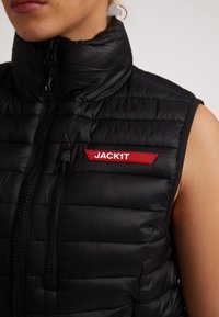 Gilet imbottito nero con colletto alto, texture trapuntata e logo rosso "JACK1T" sul lato sinistro. Presenta una chiusura frontale con cerniera e design senza maniche.