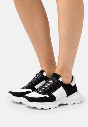Sneaker in bianco e nero con tomaia in suede e sintetico, design con lacci, suola bianca spessa e dettagli laterali.