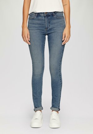 Jeans ajustados en denim azul claro, con cintura alta, diseño clásico de cinco bolsillos y puños enrollados. Combinados con zapatillas blancas.
