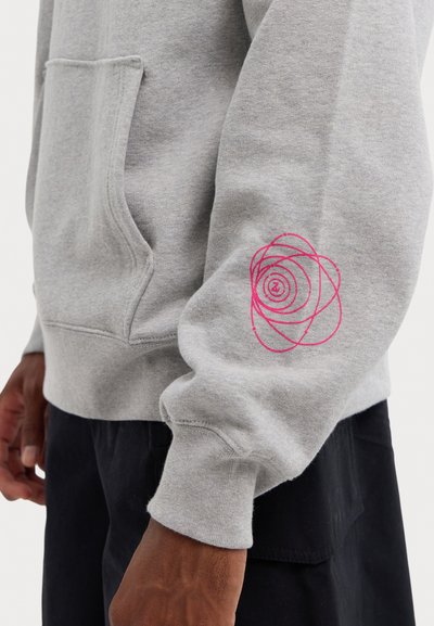 Sweatshirt gris avec une poche kangourou, orné d'un motif en spirale rose sur la manche. Texture douce, poignets côtelés et coupe décontractée.