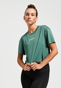 Haut de sport vert à manches courtes en tissu léger, avec un col rond et un petit logo à l'avant.